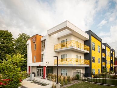 Modern apartment building with vibrant yellow and orange accents under a cloudy sky.
