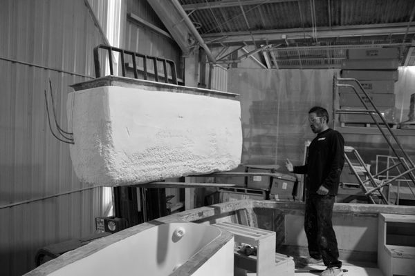 Man inspecting a foam-insulated boat hull in a workshop.