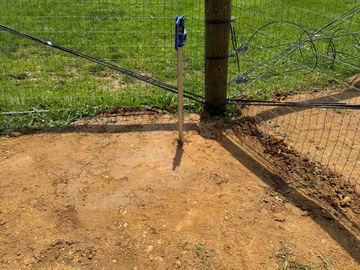 Electric fence corner with tensioners and green pasture background.