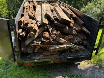 A trailer filled with old, weathered wooden beams in a green outdoor setting.