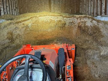 View from tractor inside a barn with hay piled up ahead.