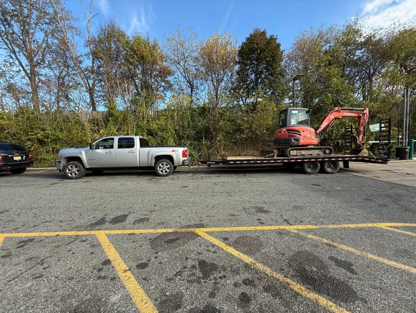 Silver pickup truck towing a flatbed trailer with a red excavator.