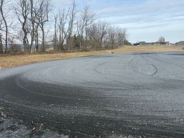 Freshly laid gravel road curving through a rural area with leafless trees.