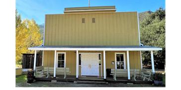 Historic yellow wooden building with a porch and white double doors.