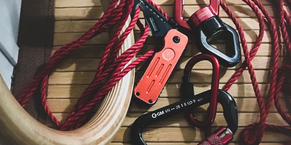 Wooden ring, cutting tool, climbing swivel, climbing carabiner, and red rope resting on a bamboo rug