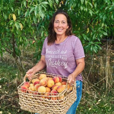 Woman holding a basket of peaches outdoors.