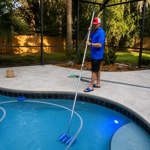 Man cleaning pool with long brush.