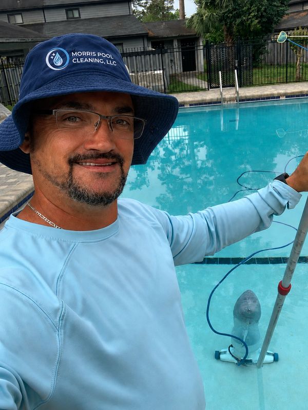 Man cleaning a pool, smiling at the camera.