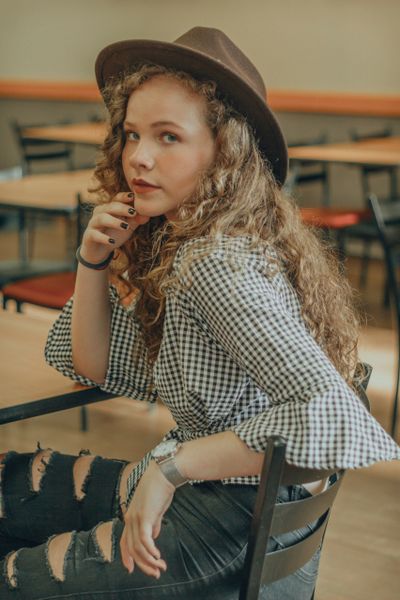 A teen girl with a hat and ripped jeans at school sitting at her desk