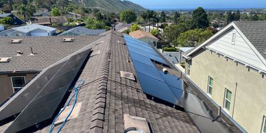 Solar panels installed on a residential rooftop with a scenic hillside background.