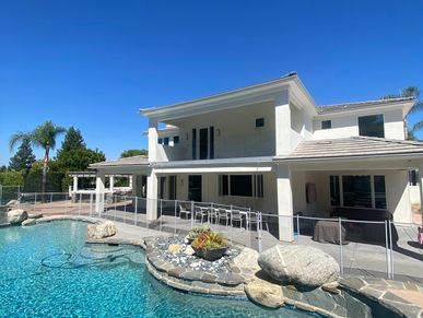 Modern two-story house with a clear blue pool under a bright sky.