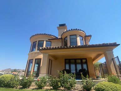 Elegant two-story house with rounded windows and a neatly manicured lawn under a clear blue sky.