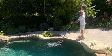 Man cleaning a backyard pool on a sunny day.
