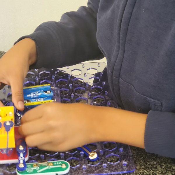 Hands assembling an electronic circuit on a blue board.