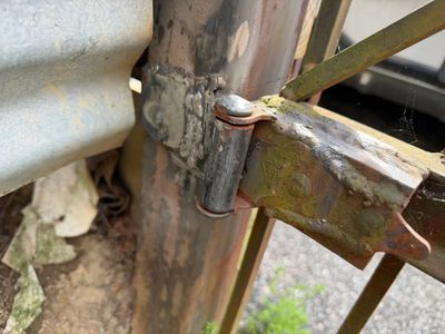 Close-up of a rusty metal gate hinge attached to a metal post.
