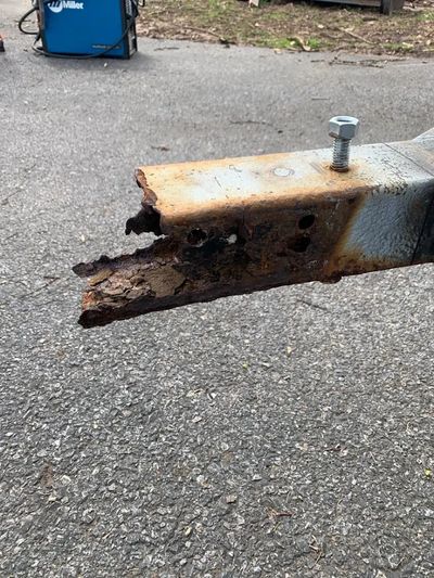 Rusty and severely corroded metal trailer hitch end outdoors on asphalt.