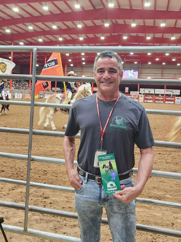 Man proudly holding an equine mortality insurance award at a rodeo event.