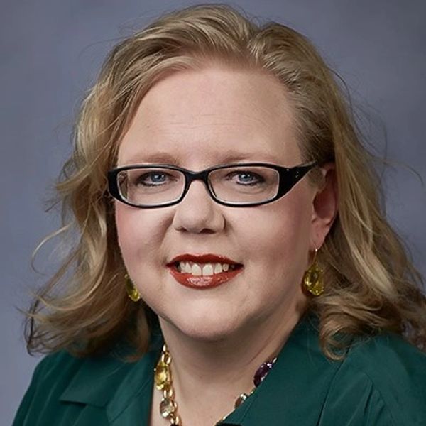 Professional woman with glasses and blonde hair smiling.