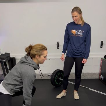 Two women in gym, one lifting a dumbbell, the other observing.