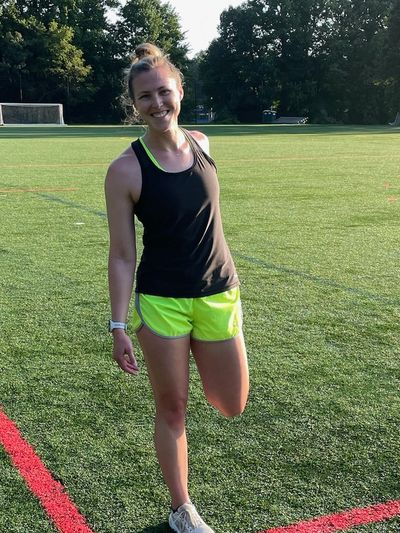 A woman stretching her leg on a sports field during sunny weather.