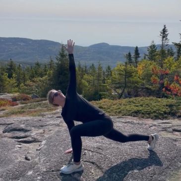 Person in black athletic wear doing a yoga pose on rocky terrain with scenic mountain views.