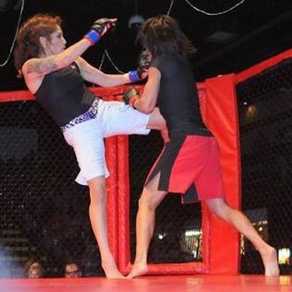 Two women engaged in a mixed martial arts fight inside a cage.