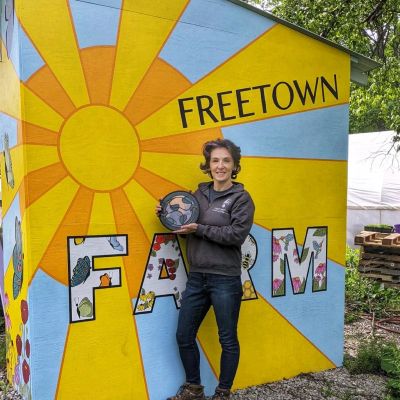Person holding a globe in front of a colorful farm mural.