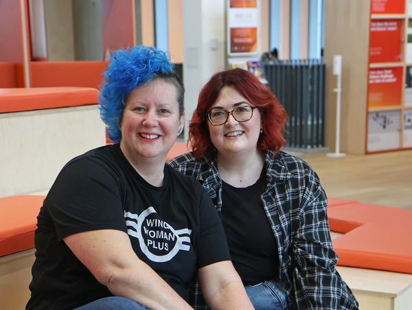 Two women sitting on orange benches smiling at the camera indoors.
