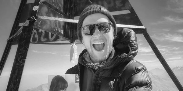 Man in winter gear smiling at a mountain summit.