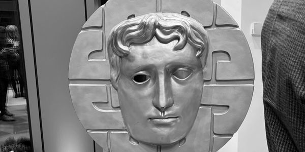 A large, ancient-style mask displayed indoors on a stand.