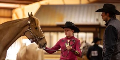 Young rider training a horse under supervision indoors.