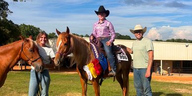 A young rider on a ribbon-adorned horse with two adults and another horse.