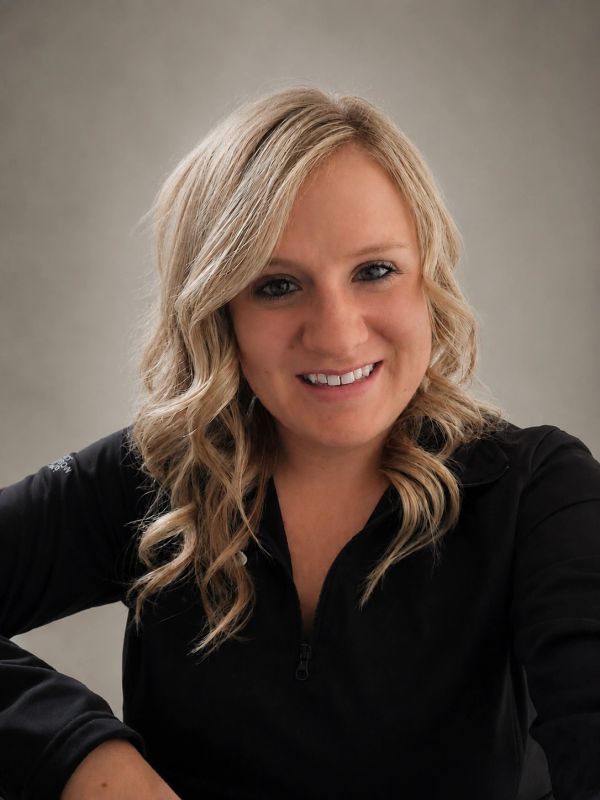 Smiling woman with blonde curly hair wearing a black top against a plain background.