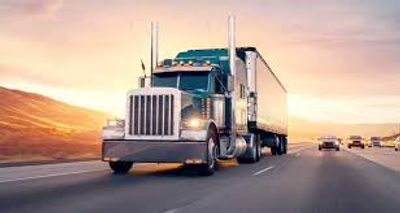 A large semi-truck driving on a highway during sunset.