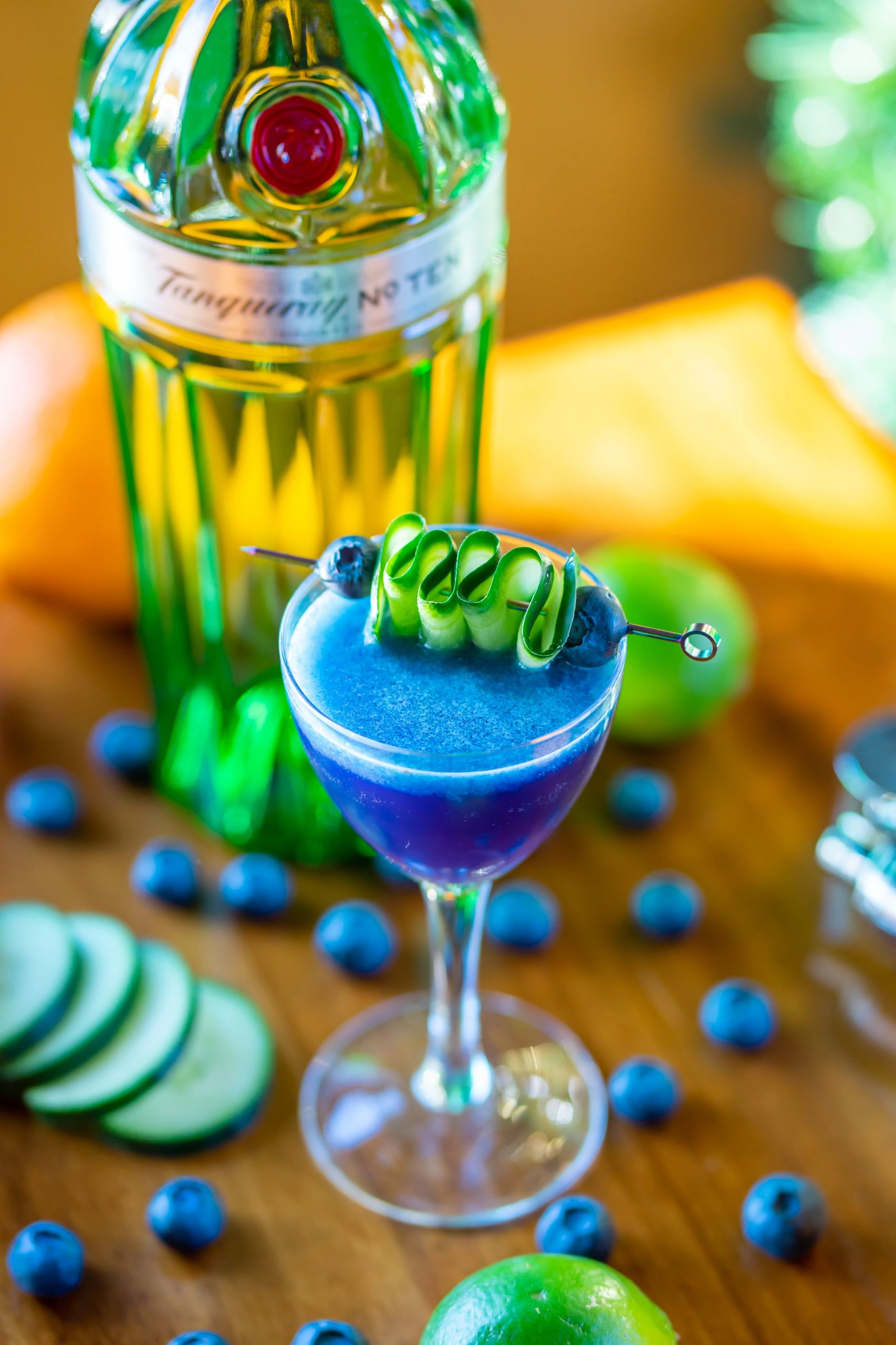 Blue cocktail with cucumber and blueberries, accompanied by a gin bottle.