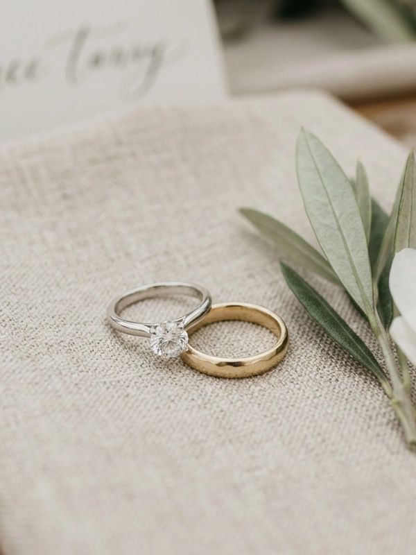 Two elegant rings, one silver with a diamond and one simple gold, resting on a textured fabric.