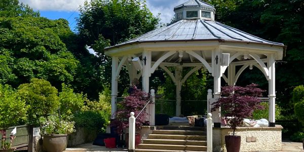White gazebo surrounded by potted plants and greenery.