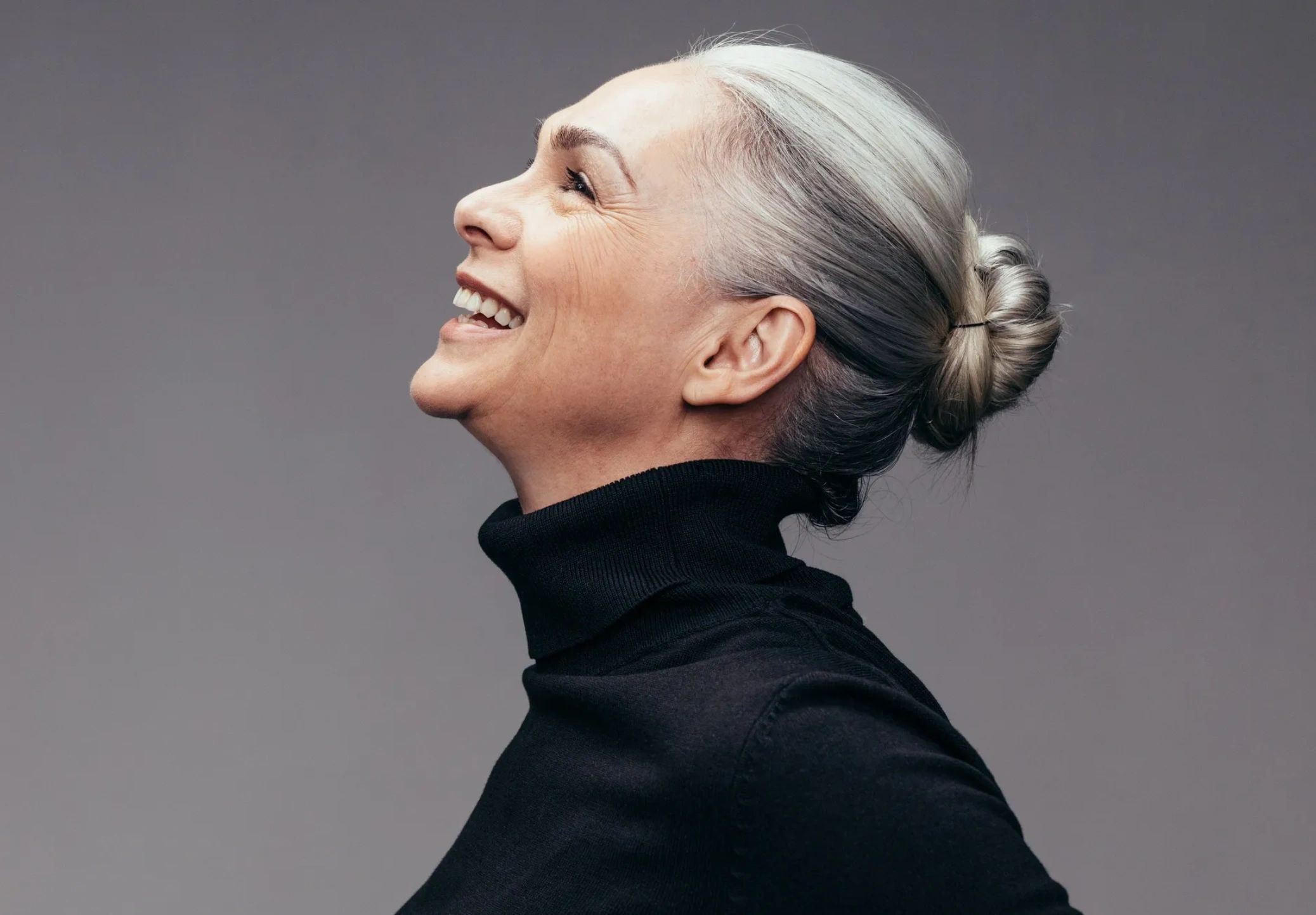 Side profile of a smiling elderly woman with silver hair in a bun.