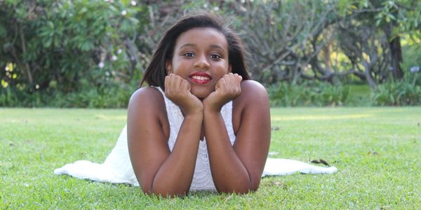 A woman in a white dress lies on green grass, smiling at the camera. following her weight loss programme