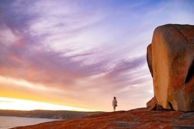 Person standing on rocky terrain at sunset.