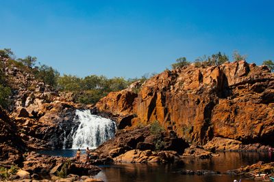 A waterfall cascading over rocks into a pool under a clear sky.
