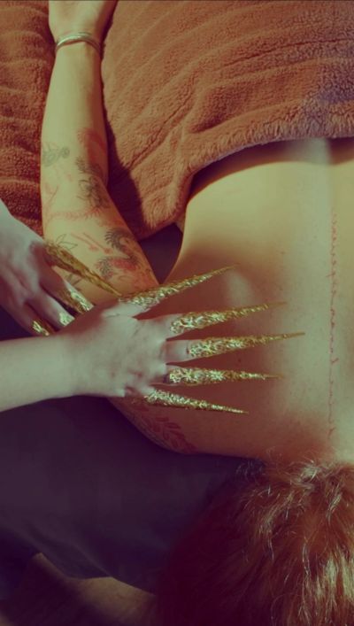 Person with gold metallic long nails touching another person's tattooed arm.