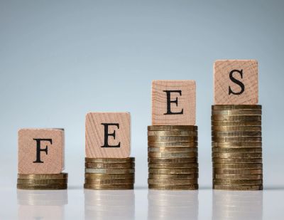 Wooden blocks on coin stacks spell 'FEES'.