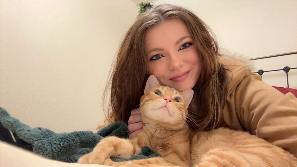 Young woman smiling with a ginger cat on a bed.