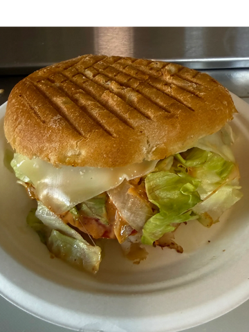 Grilled chicken sandwich with lettuce and melted cheese on a white plate.
