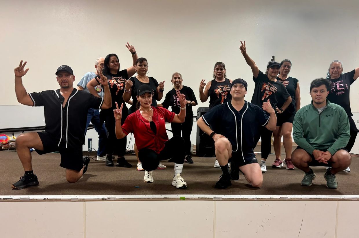 Group photo of diverse people posing on stage, showing peace signs and thumbs up.