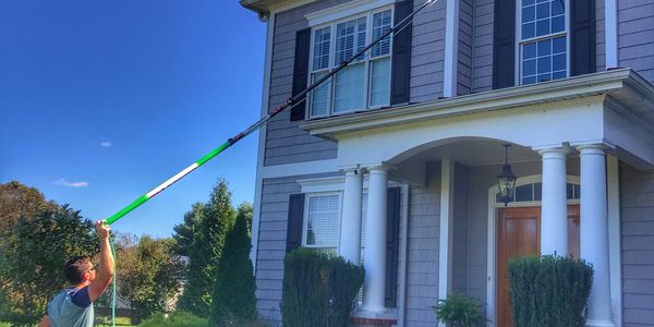 Man scrubbing third-story window from ground with long pole