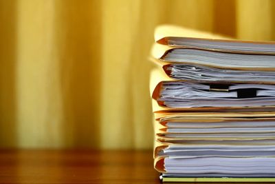 Stack of organized paper files on a wooden surface with a yellow background.