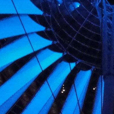 Large umbrella-like structure suspended from cables and lit in blue, seen from below