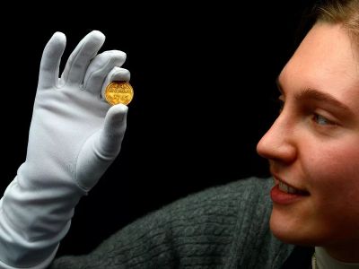Person examining a gold coin with white gloves.